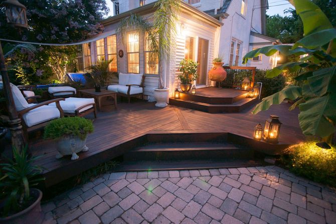 Cozy lit patio with white seating, stone steps, lanterns, and tropical plants at dusk
