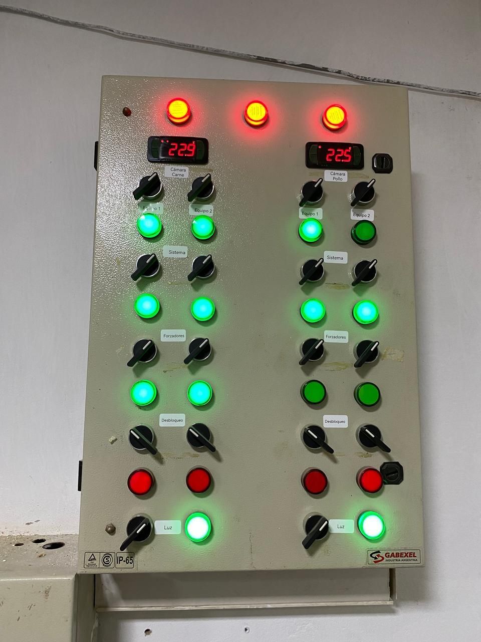 Panel de control mural con pantallas digitales rojas y filas de luces indicadoras verdes y rojas iluminadas.