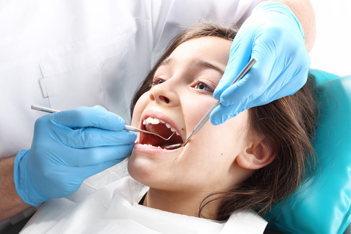 Dentist examining a patient’s open mouth with gloved hands and dental tools