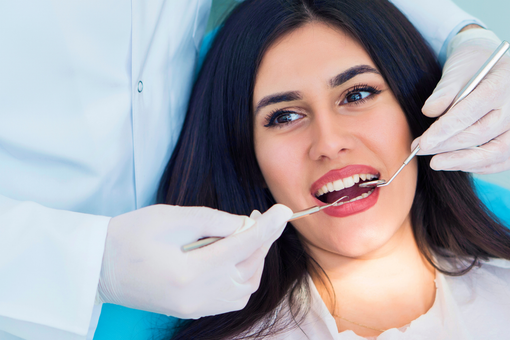 Dentist examining a smiling patient’s mouth with dental tools and gloves