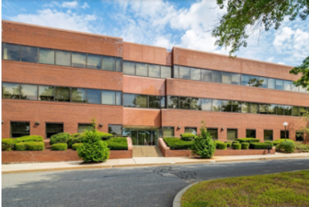 Red brick office building with multiple rows of windows, landscaping, and a paved road.