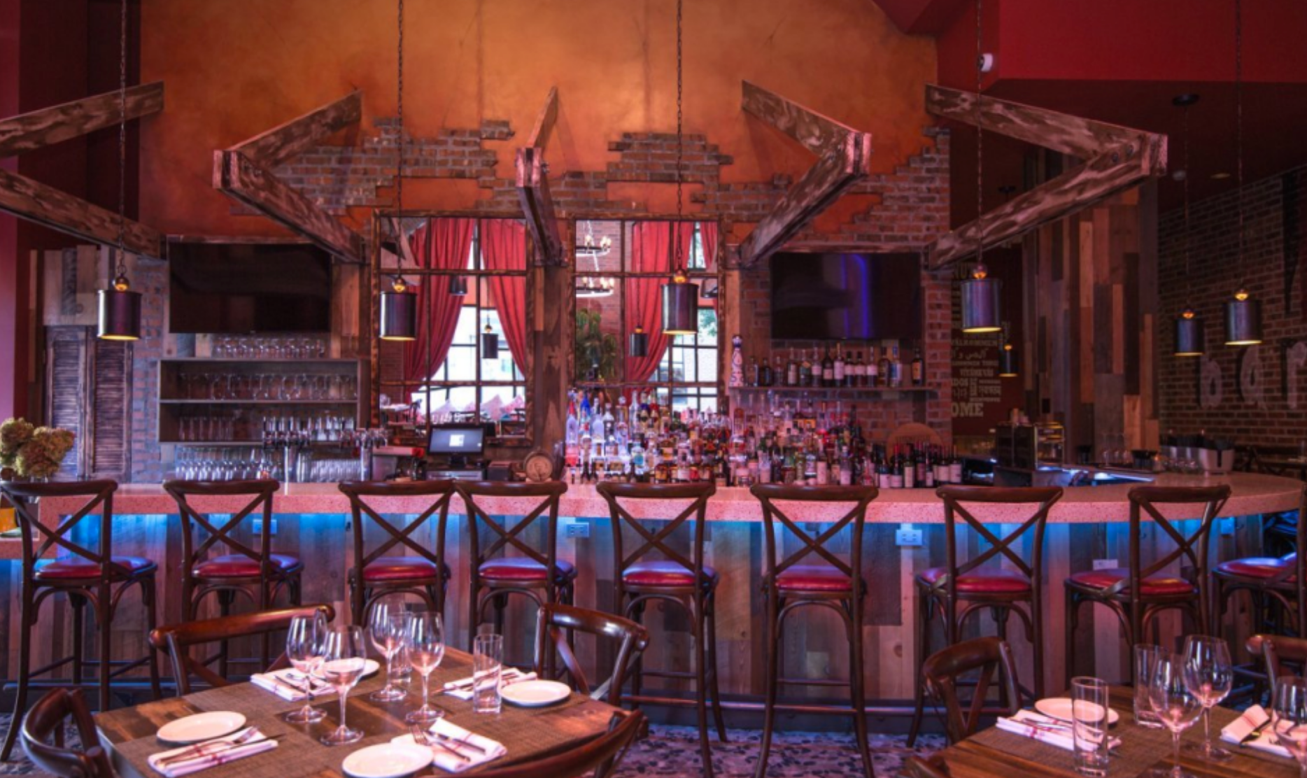A restaurant bar with red chairs, a lit bar, and decorative wooden accents.