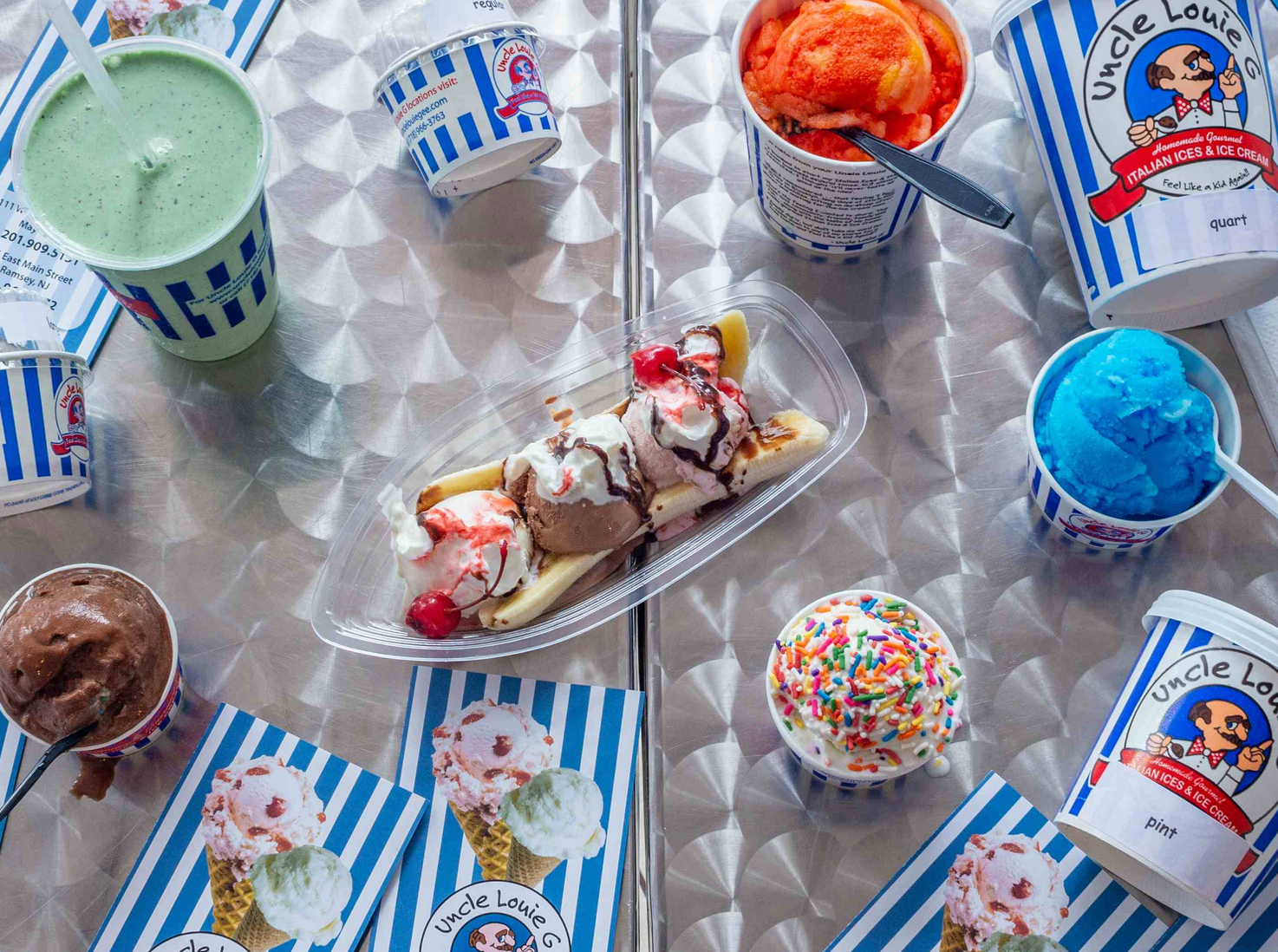 Ice cream treats: banana split, shakes, and cups of various flavors on a striped table.