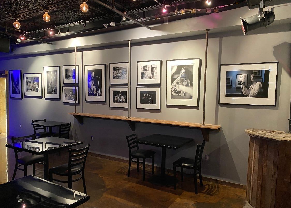 A bar or restaurant interior with tables, chairs, artwork on the wall, and decorative lights.