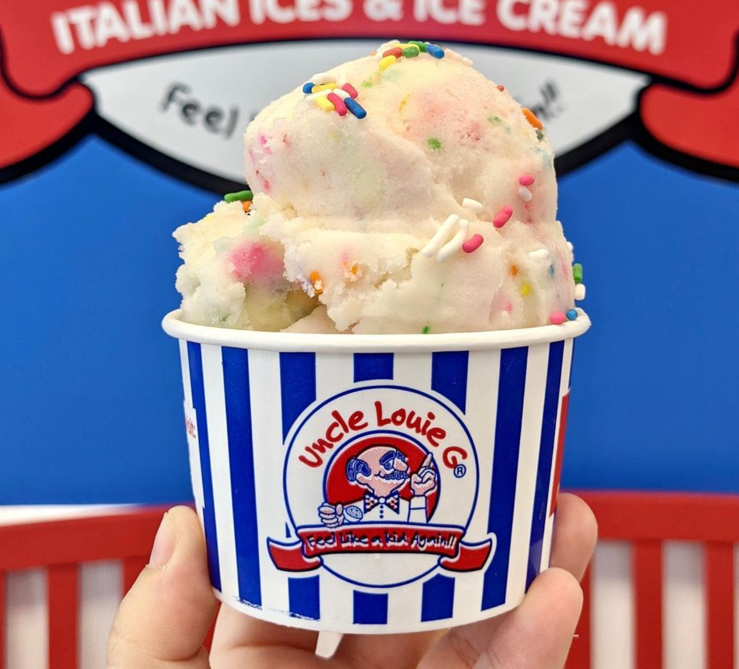 Ice cream in a blue-and-white striped cup, held by a hand. Sprinkles top the white ice cream. 