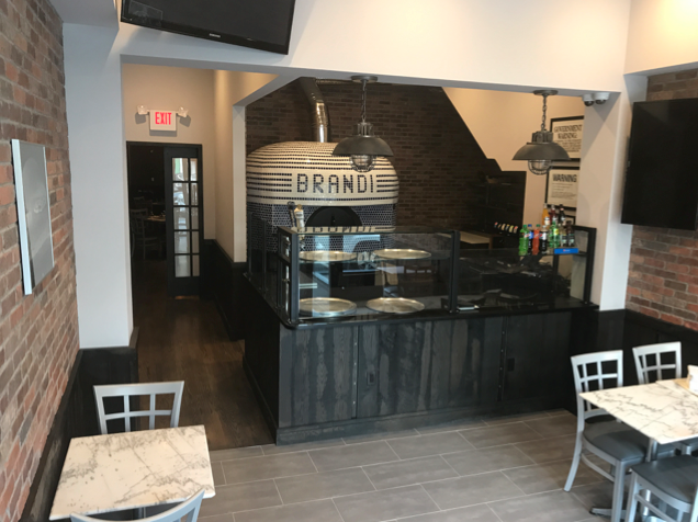 Interior of a pizzeria with a brick wall, marble tables, and a pizza oven that says 