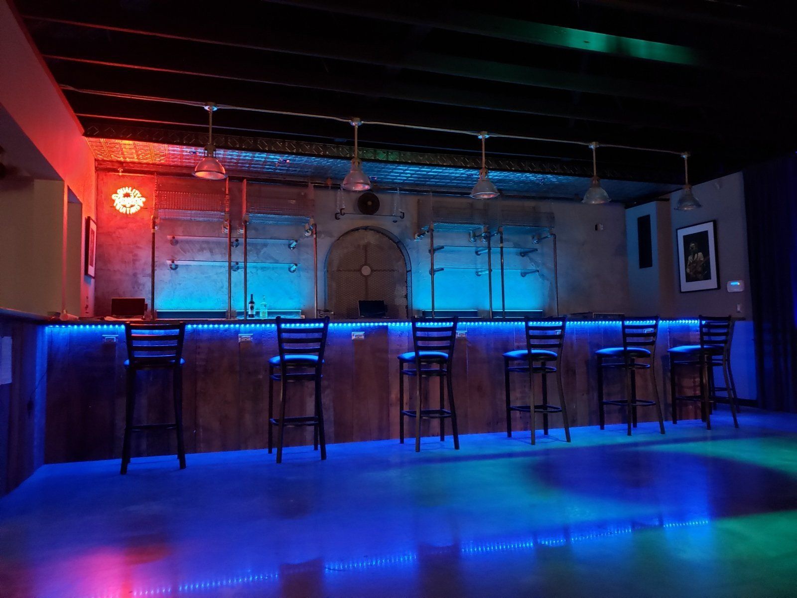 Bar with blue and red lighting, high stools, exposed brick and concrete walls.
