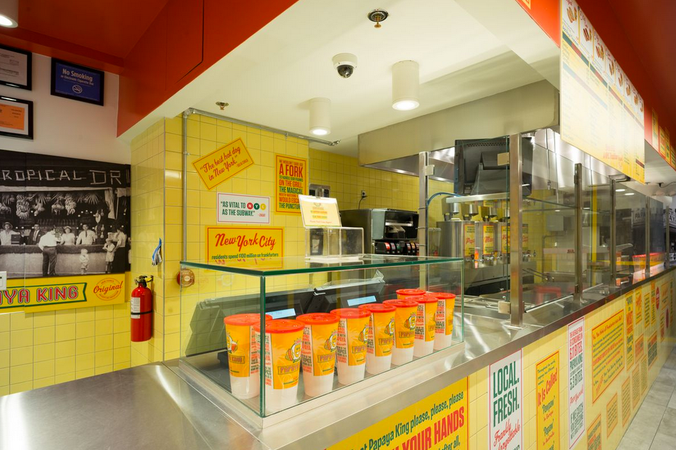 Interior of a fast food restaurant with counter, drinks, and food preparation area. Yellow and orange color scheme.