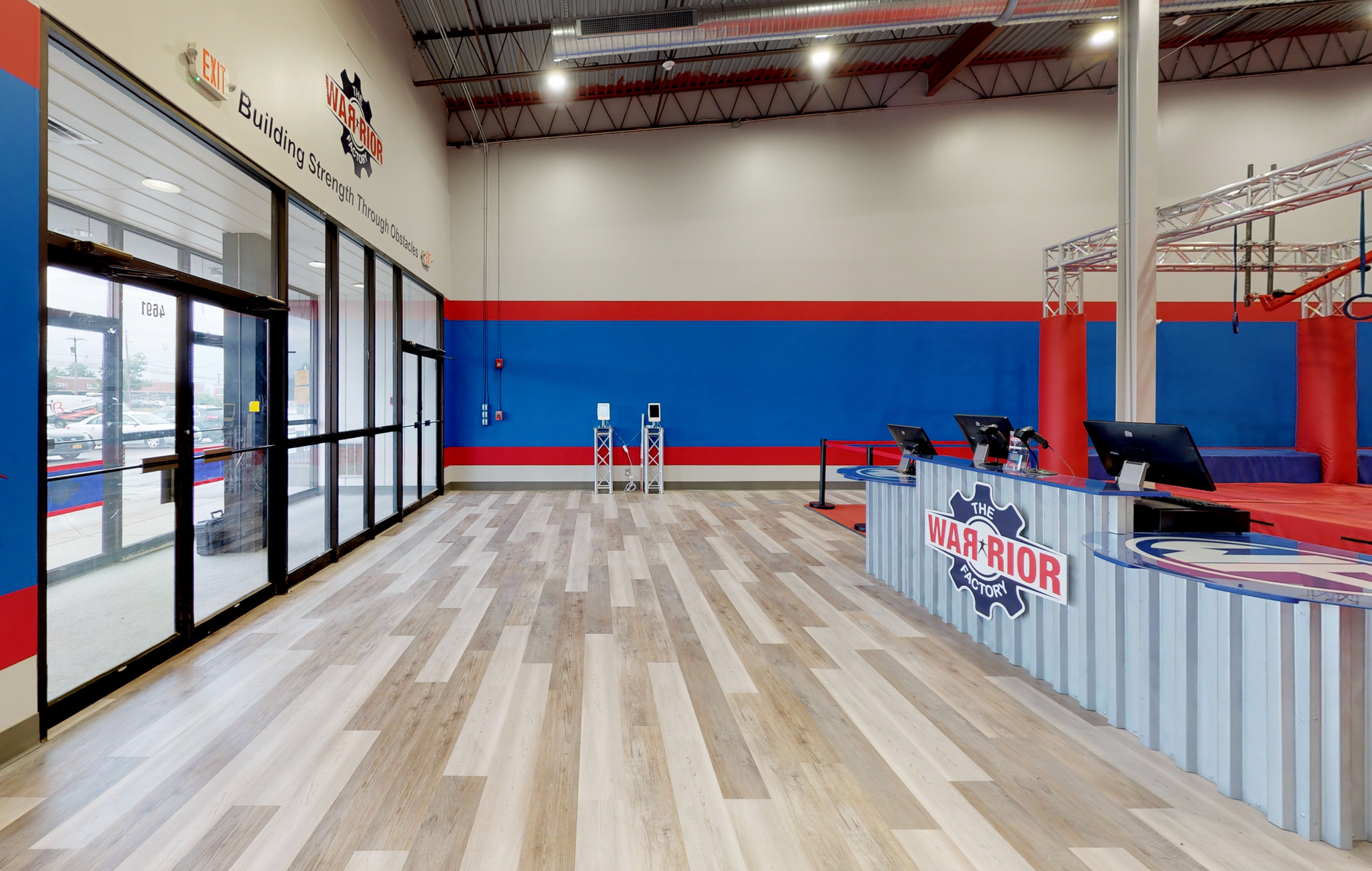 Entrance to a Ninja Warrior gym with a wooden floor, check-in counter, and blue and red walls.