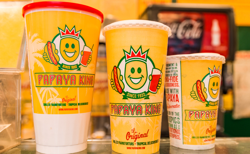 Papaya King cups in various sizes, yellow with logo of a smiling hotdog holding a drink.
