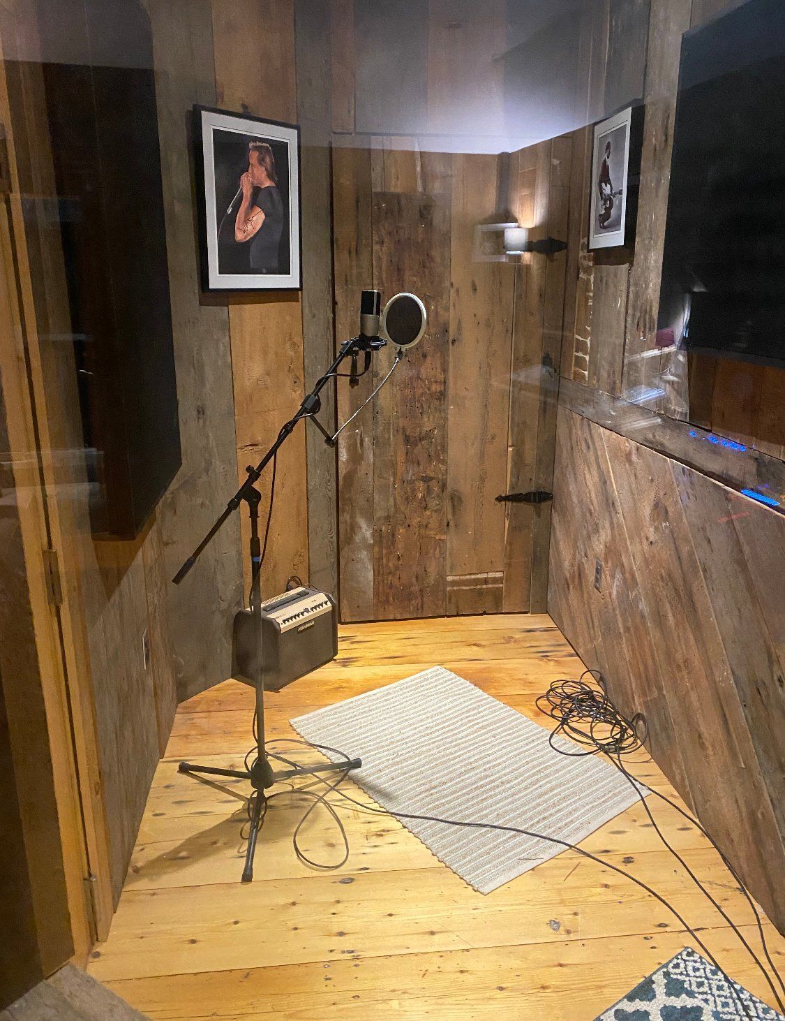 Recording booth with microphone, rug, wood paneling, art on walls, door.