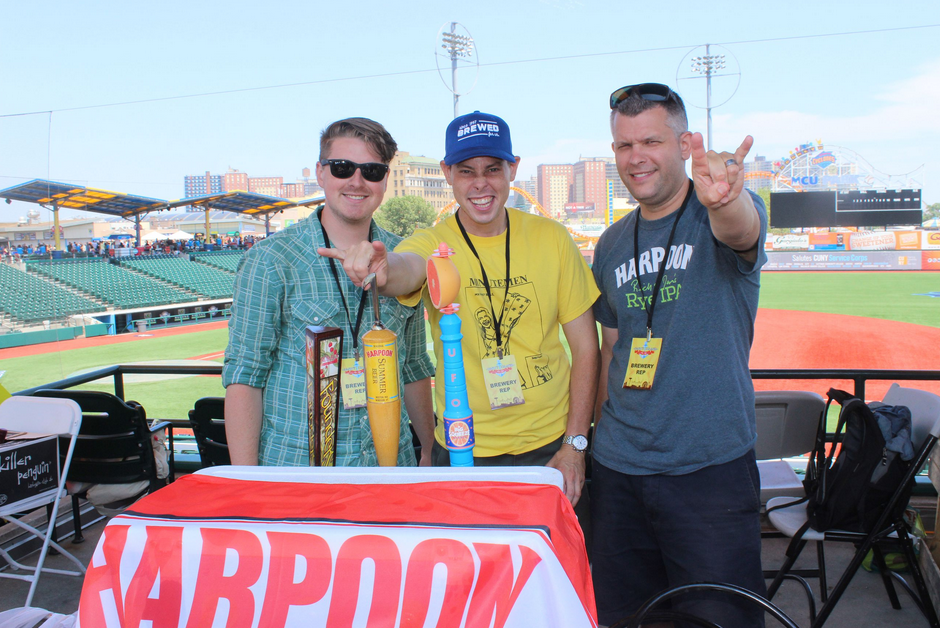Three men at a baseball game holding food, smiling, and gesturing. Table with 