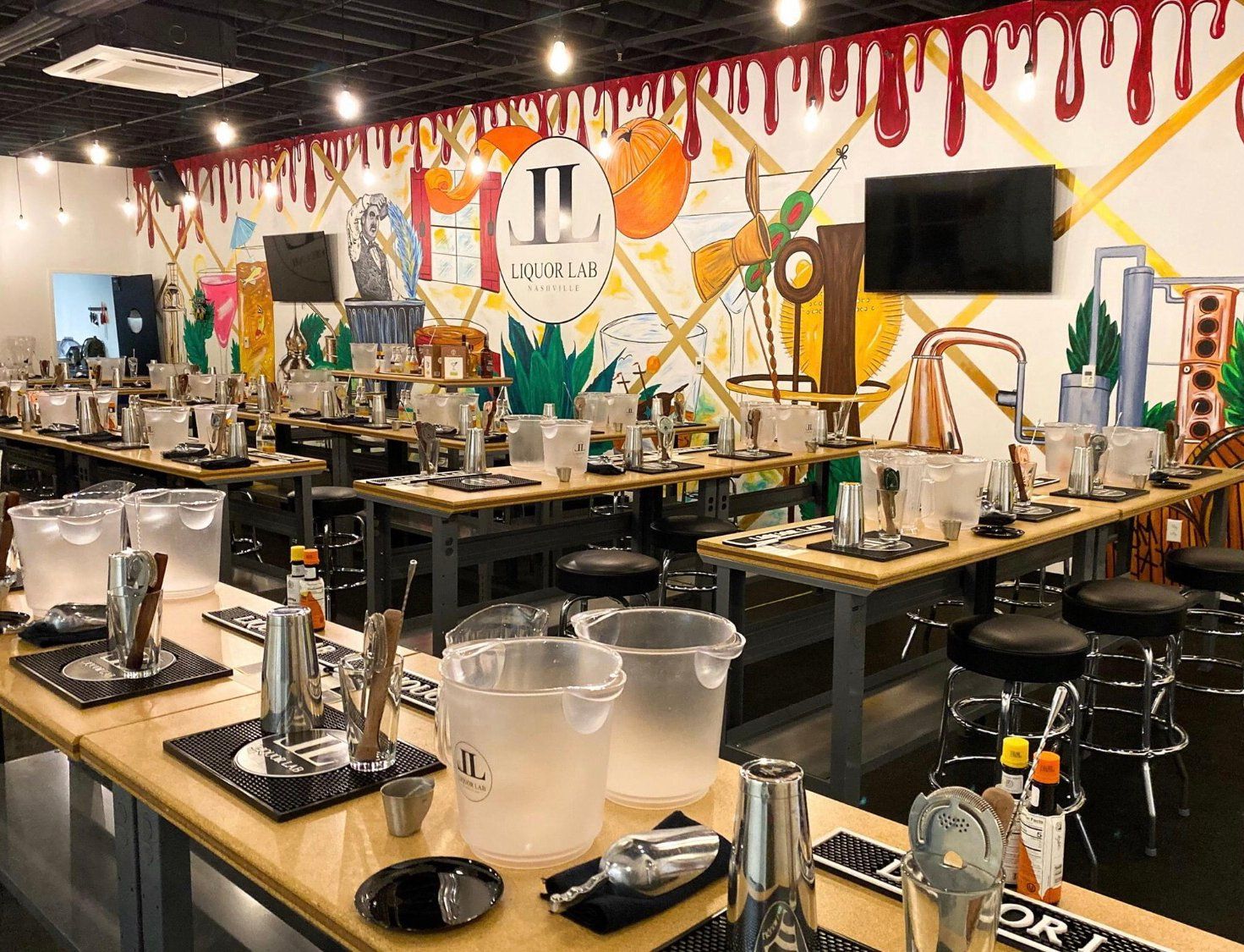 Cocktail-making class: rows of stations with shakers, ice buckets, and tools. Mural backdrop, red paint drip accents.