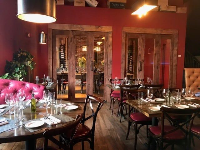 Elegant restaurant interior with tables set for diners. Red walls, wooden doors, and seating.