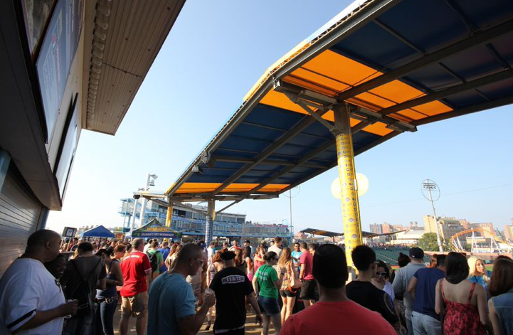 Crowd of people near a pier, under a blue and yellow awning, on a sunny day.