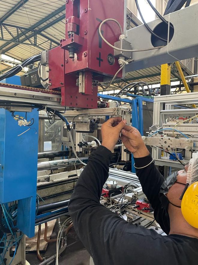 Un técnico con protección auditiva amarilla ajusta el equipo de una máquina de fábrica bajo una unidad superior roja.