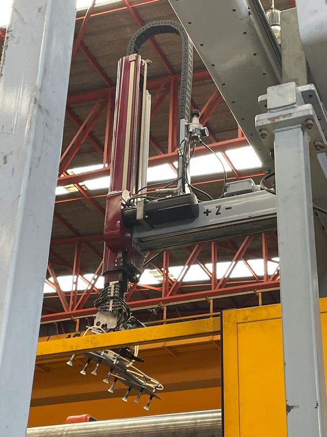 Máquina industrial suspendida en una fábrica con mangueras a rayas y una viga superior amarilla