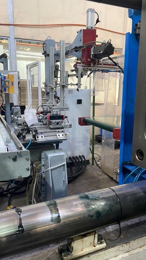 Máquina industrial en un taller, con tuberías metálicas y un brazo robótico rojo ensamblado.