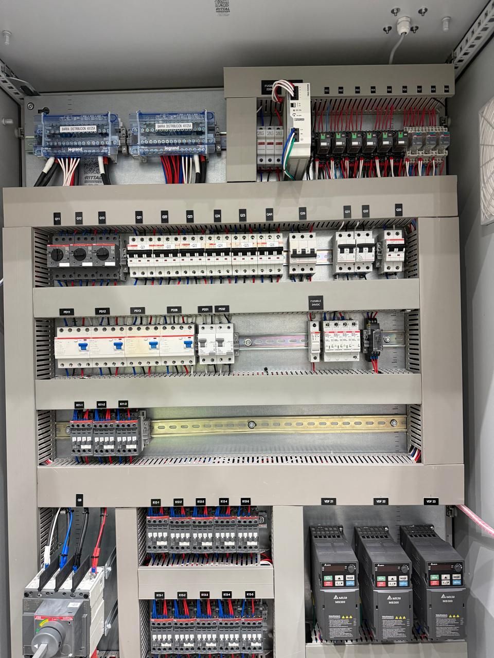 Panel de control eléctrico abierto con disyuntores, relés y cableado dentro de un gabinete metálico.