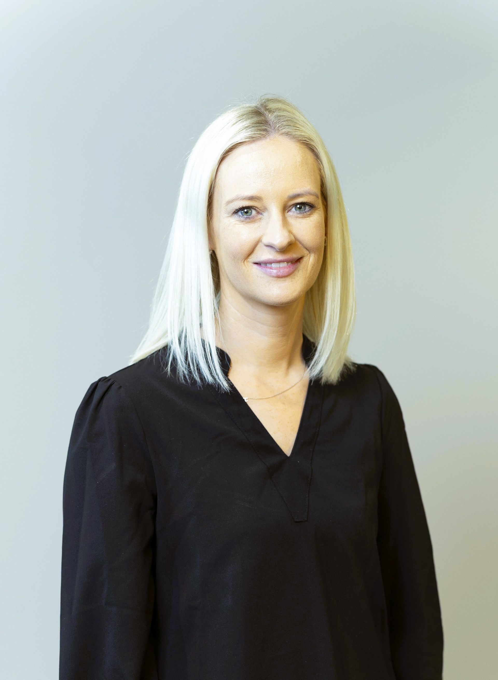 Portrait of a smiling blonde person in a black blouse against a light gray background