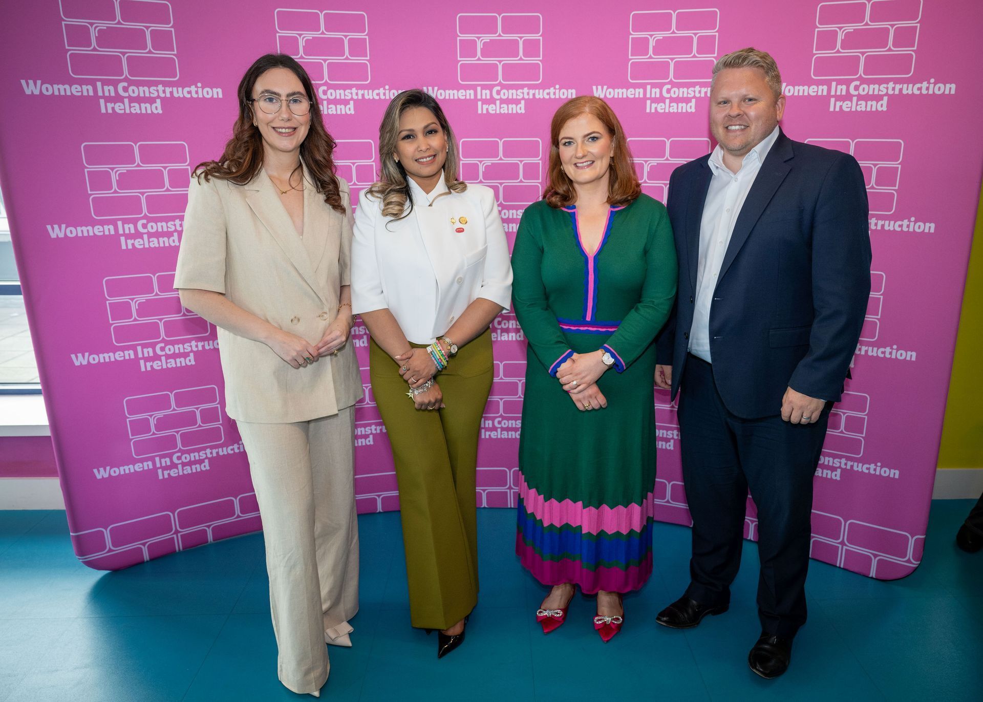 Four people posing before a pink Women in International Security backdrop at a formal event.
