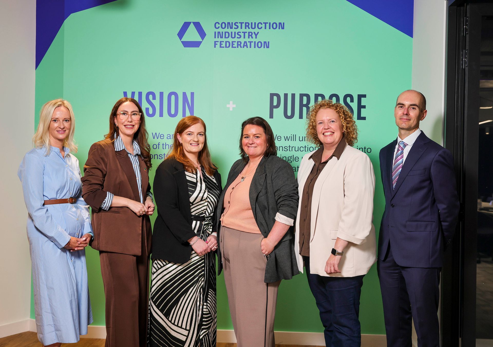 Six people posing on stage at a “Vision Purpose” event with a company backdrop.