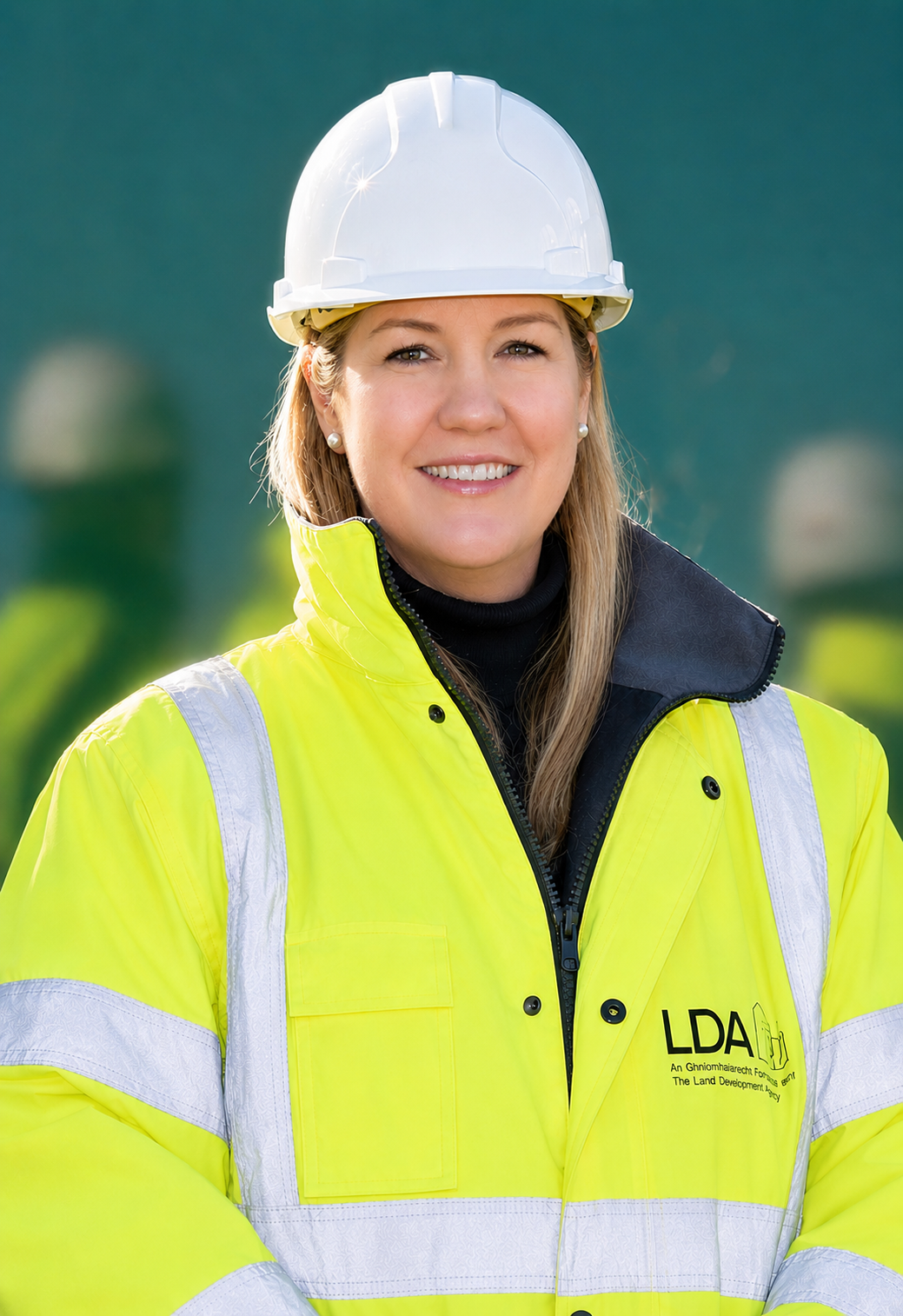 Smiling worker in a white hard hat and neon yellow safety jacket with reflective stripes, standing outdoors