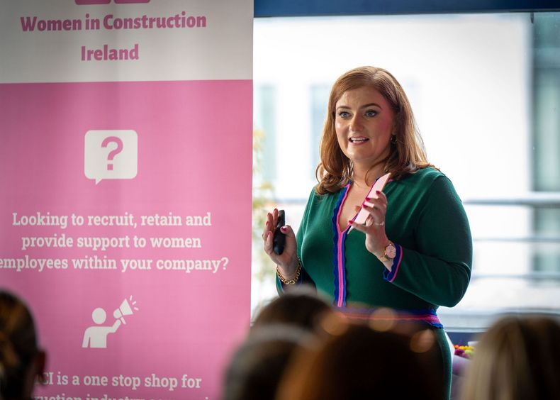 Speaker presenting beside a Women in Construction Ireland banner at a conference