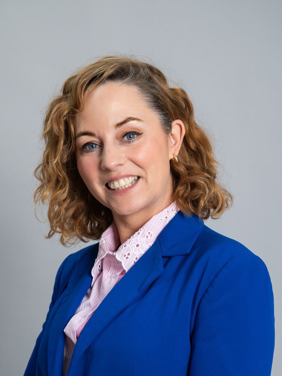 Smiling professional in a blue blazer and pink shirt against a light gray background