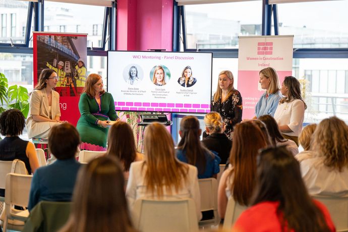 Panel discussion in a bright event space with audience facing a presentation screen