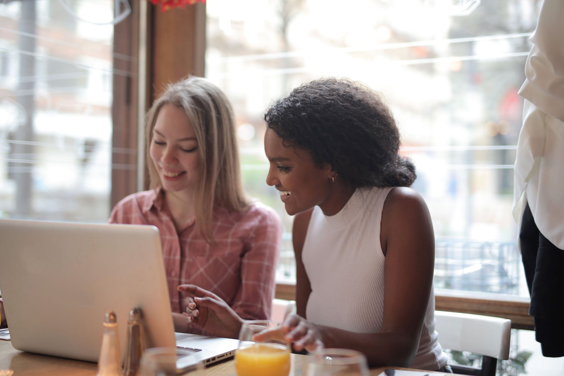 Two people collaborating at a laptop in a bright café, smiling and reviewing something on screen