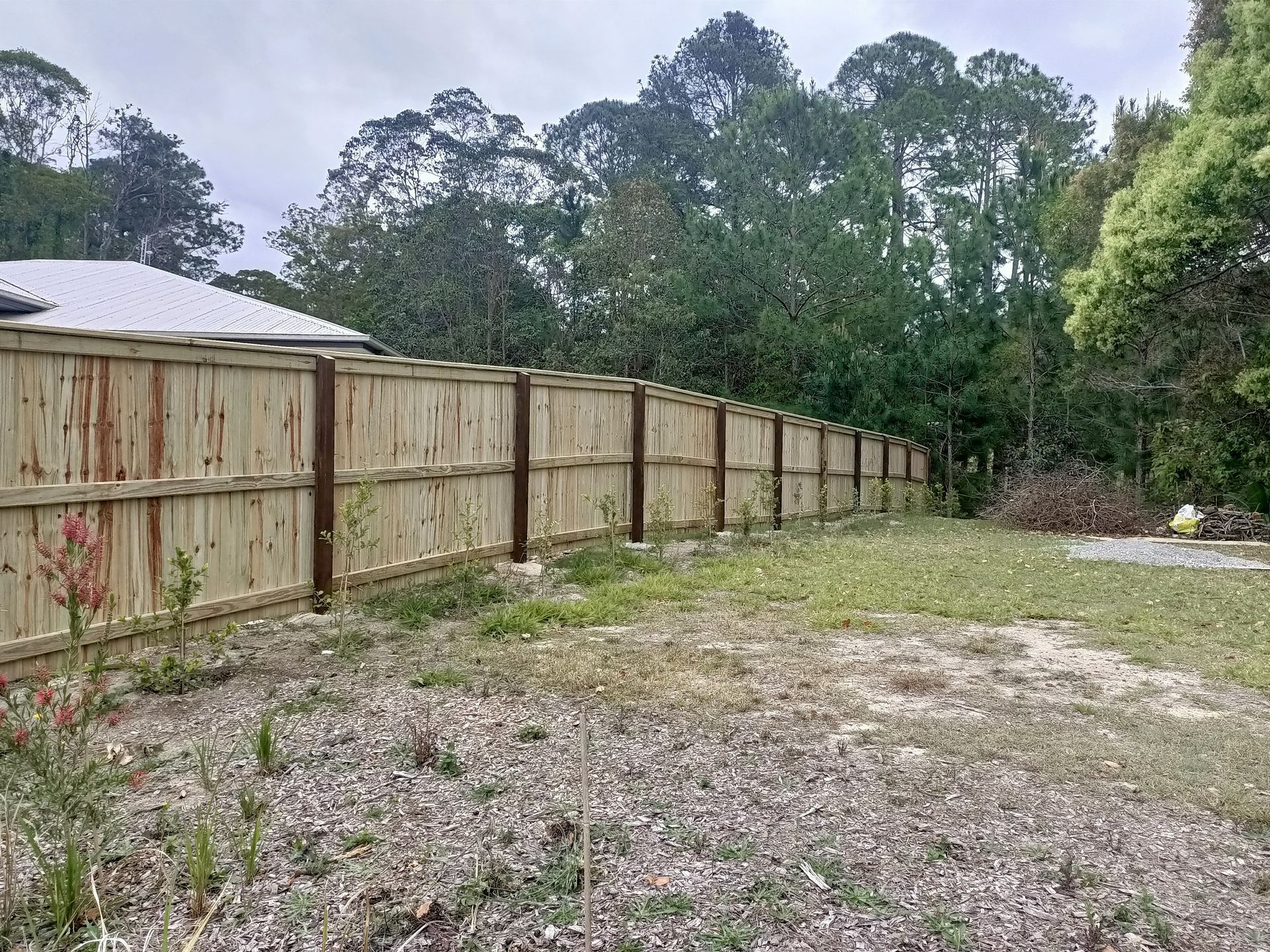 Wooden Fence Along A Gravel Lot With Trees And A Small House In The Background — Quality Fences 4 U in Gympie, QLD