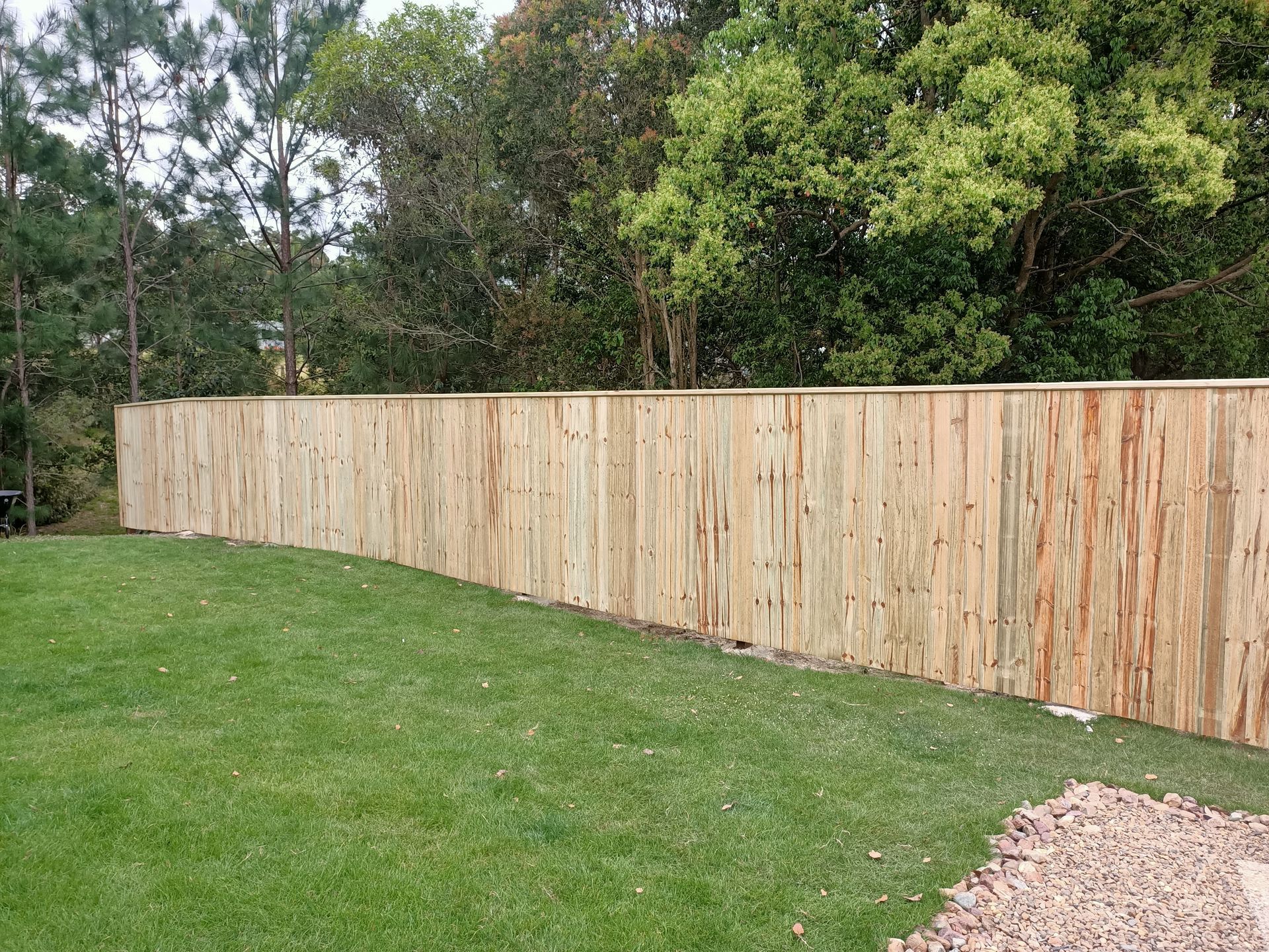Long Wooden Fence Bordering A Green Lawn With Trees In The Background — Quality Fences 4 U in Gympie, QLD