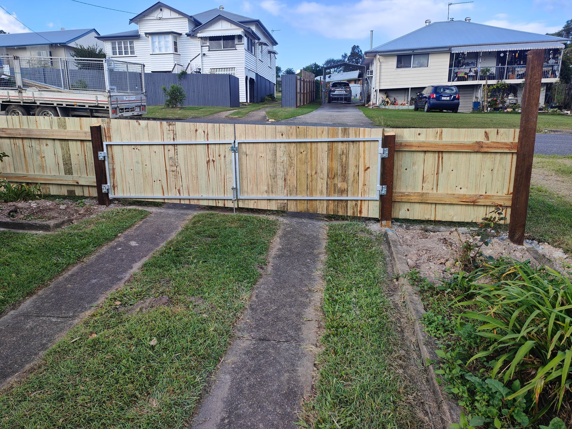 Wooden Driveway Gate Across A Grassy Path, With Houses In The Background — Quality Fences 4 U in Gympie, QLD