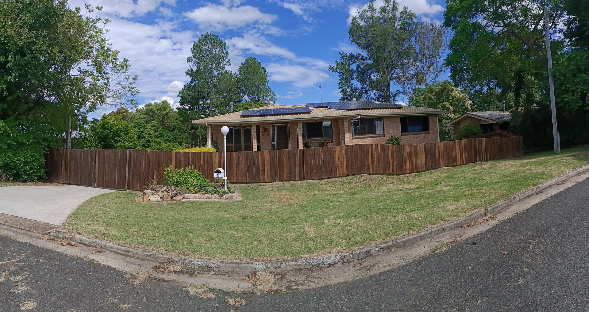 Single-story House Behind A Wooden Fence On A Corner Lot, With Grass, Trees, And A Blue Sky — Quality Fences 4 U in Gympie, QLD