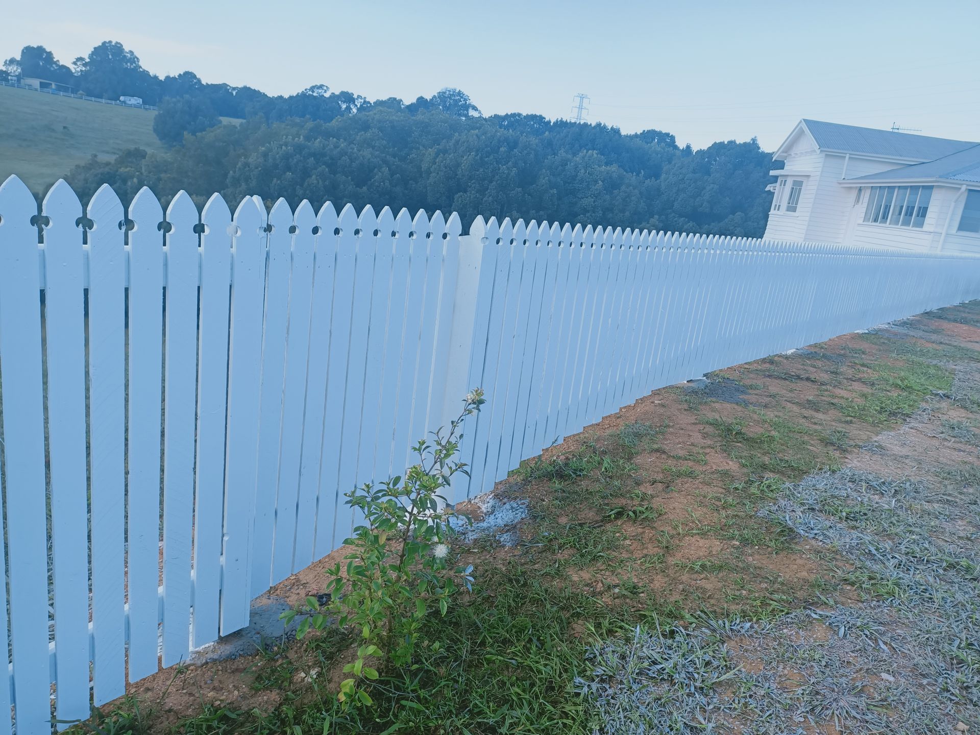 White Picket Fence Beside A Gravel Road, With Trees And A House In The Background — Quality Fences 4 U in Gympie, QLD