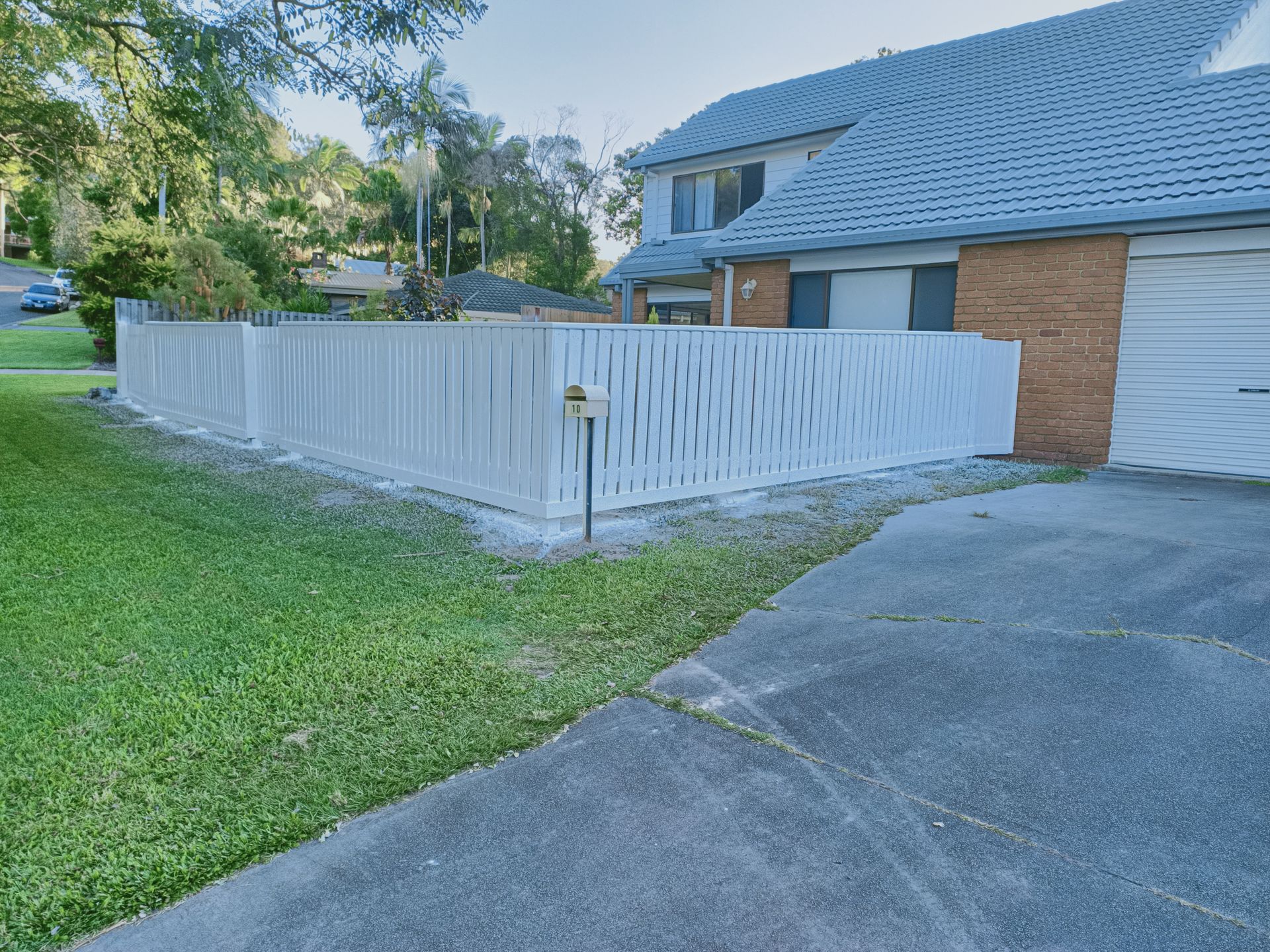 White Fence Beside A Driveway And Garage Next To A Brick House, With A Green Lawn And Trees — Quality Fences 4 U in Gympie, QLD