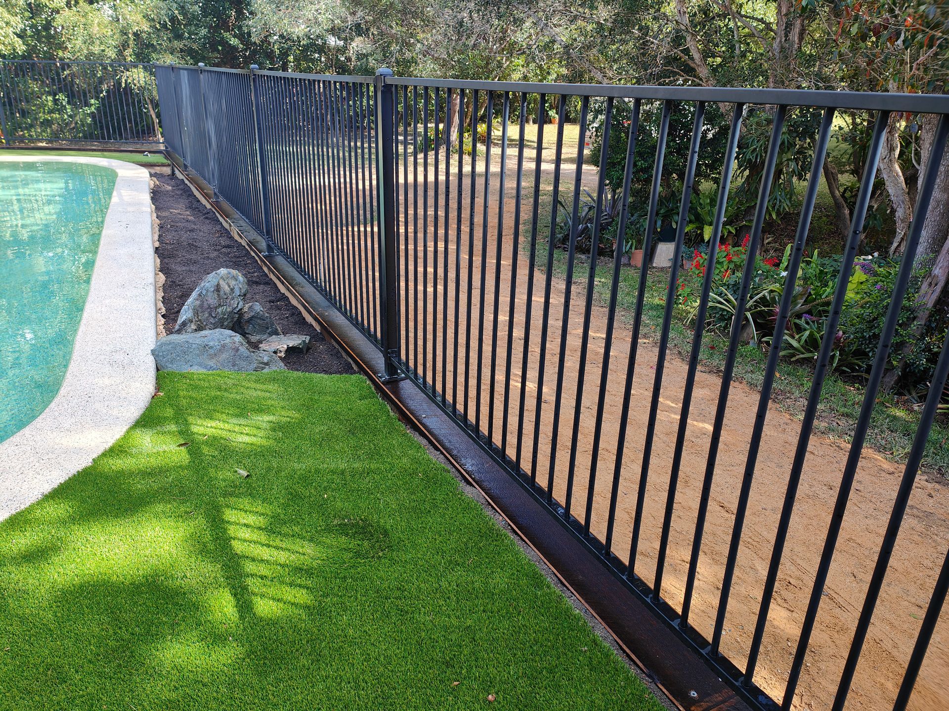 Black Metal Fence Beside A Turquoise Pool And Green Lawn In A Landscaped Yard — Quality Fences 4 U in Gympie, QLD
