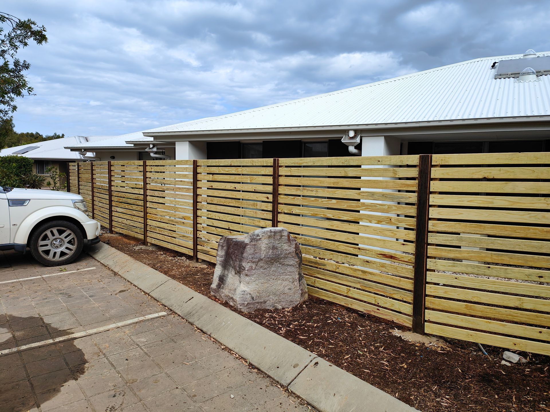 White SUV Beside A Wooden Slat Fence And Concrete Parking Area Under A Cloudy Sky — Quality Fences 4 U in Gympie, QLD