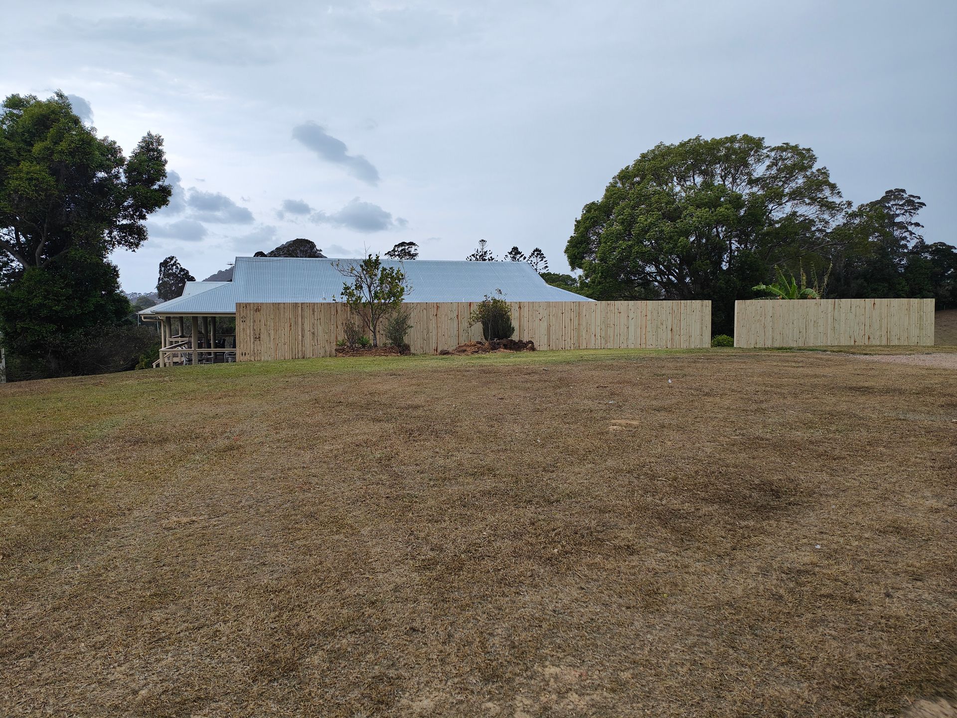 Rural Yard With A Beige Fence, Blue-roofed House, Trees, And A Dry Grassy Field Under Cloudy Sky — Quality Fences 4 U in Gympie, QLD
