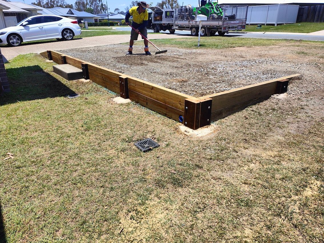 Raised Wooden Garden Bed In A Grassy Yard, With A Person Standing Beside It And Parked Cars In The Background — Quality Fences 4 U in Gympie, QLD