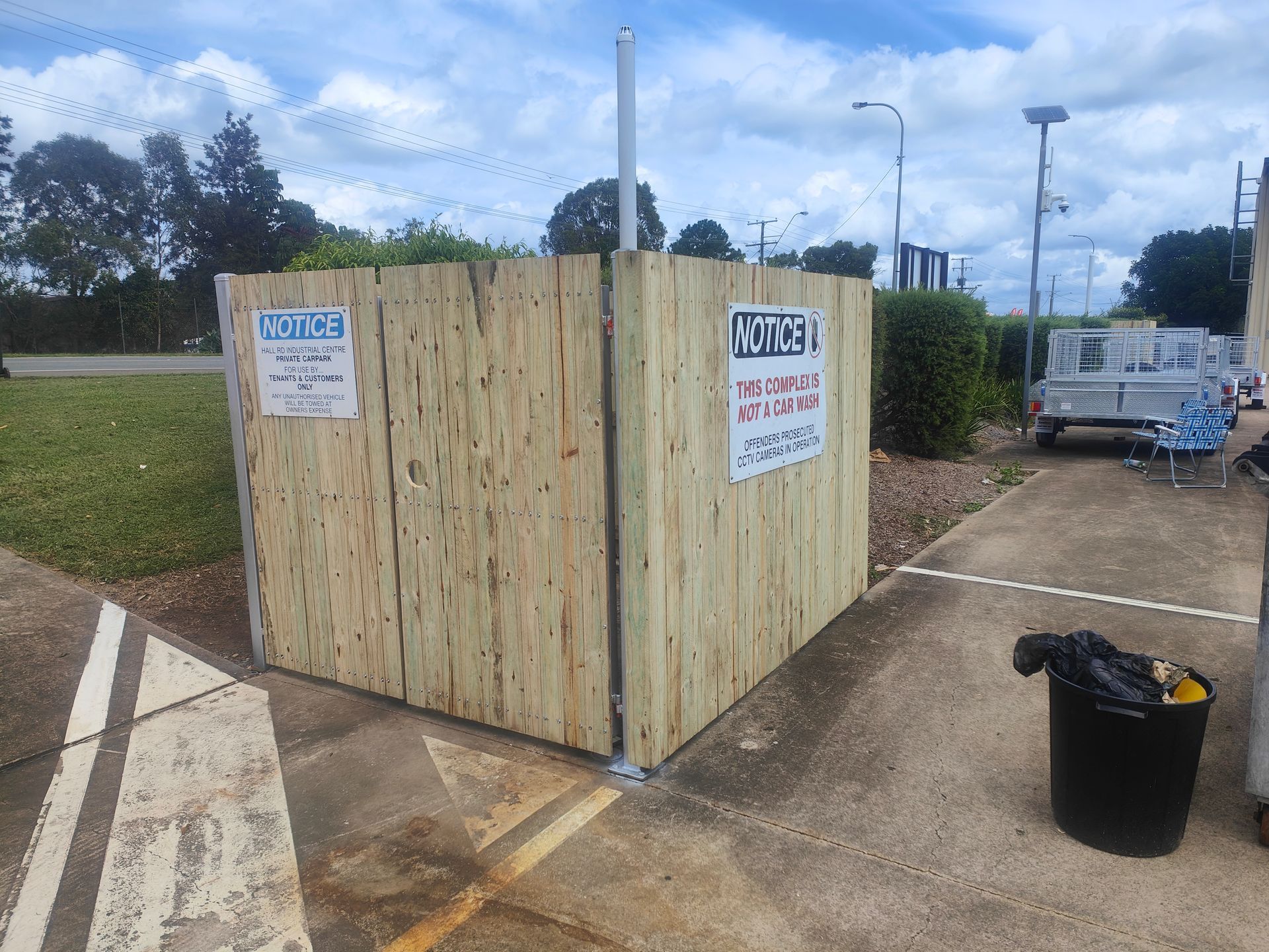 Wooden Fenced Waste Enclosure With Warning Signs Beside A Pavement And Trash Bin In A Parking Area — Quality Fences 4 U in Gympie, QLD