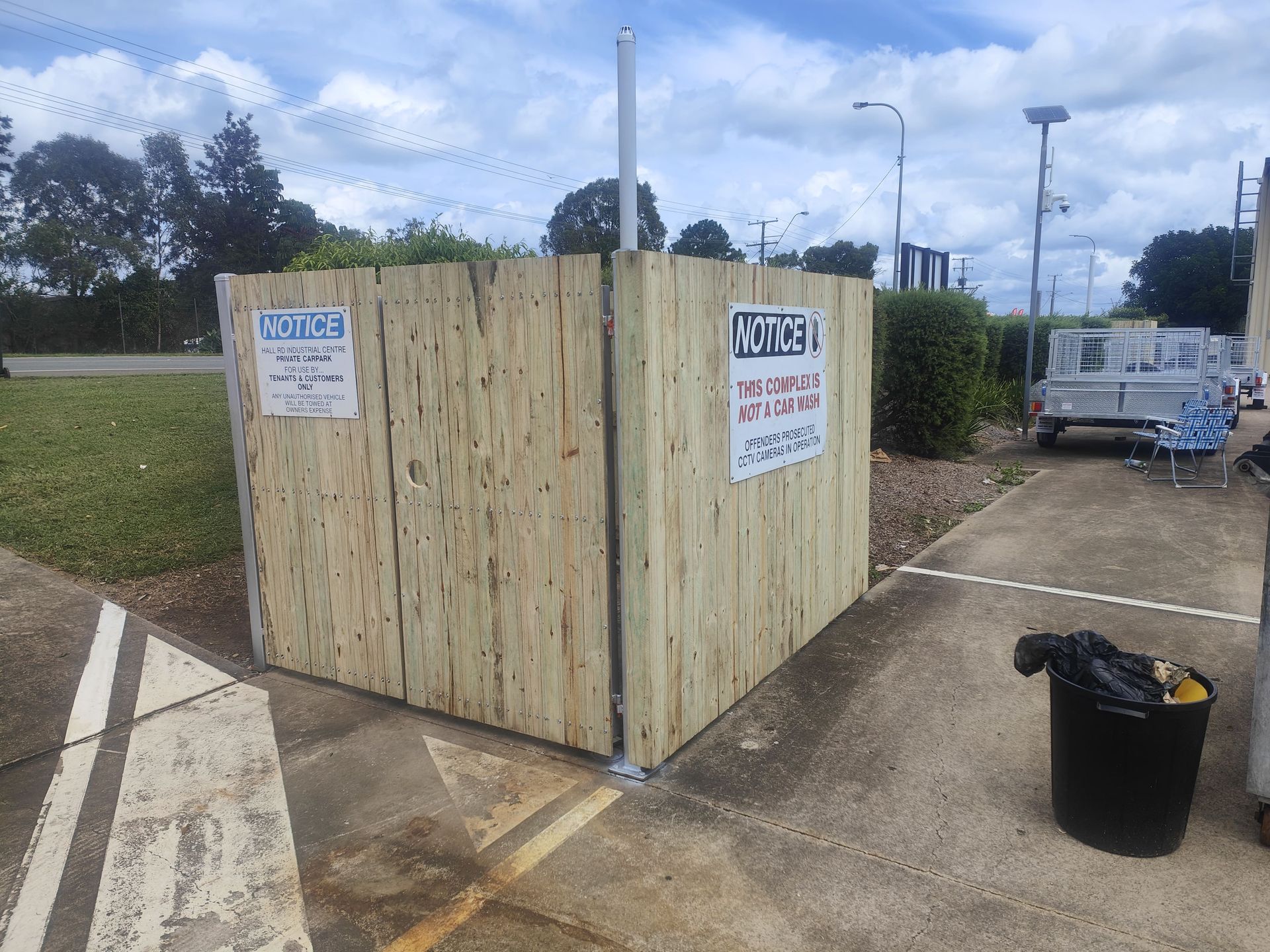 Wooden enclosure with signs, next to a sidewalk and a trash can, with a trailer in the background — Quality Fences 4 U in Gympie, QLD