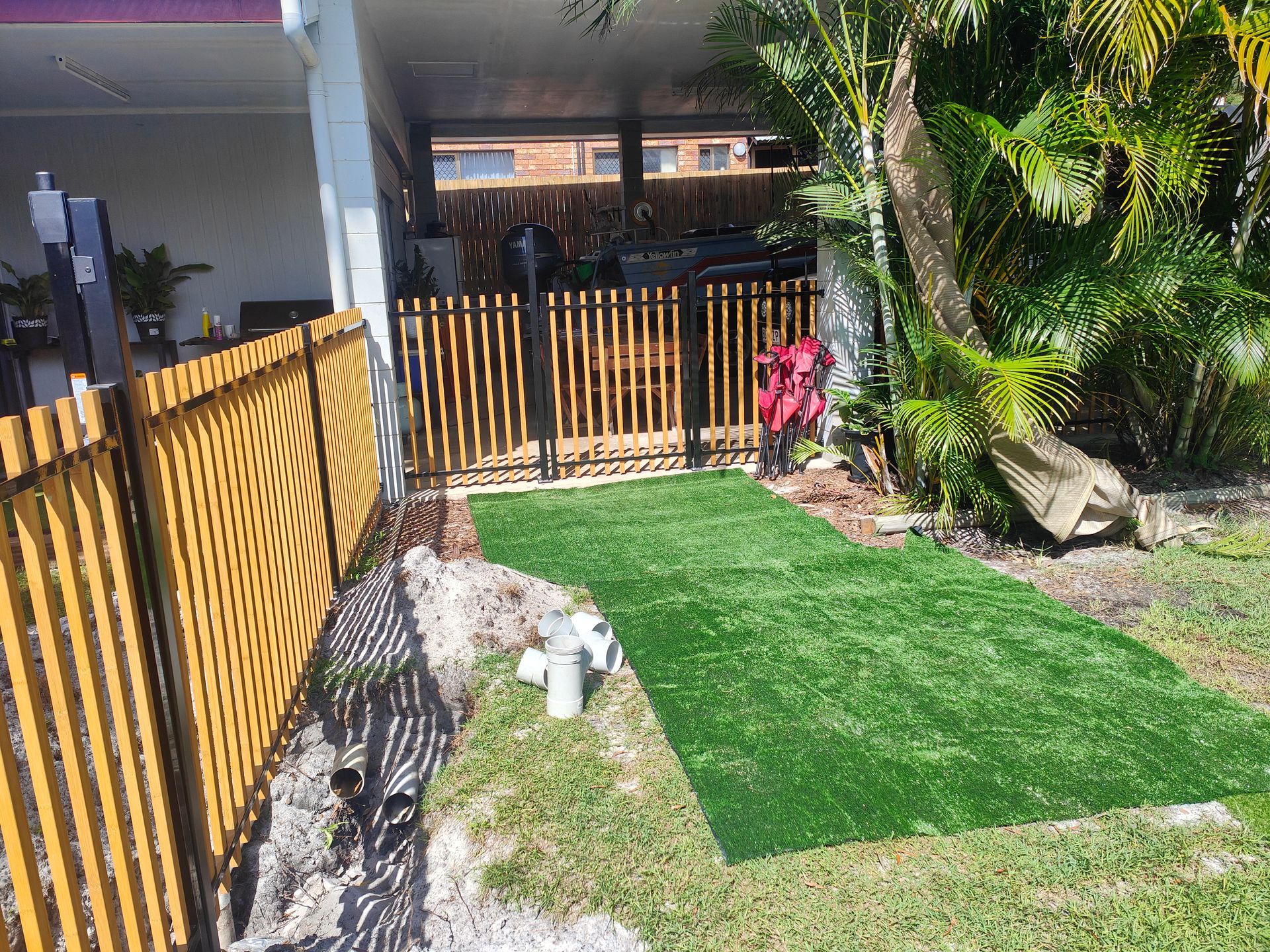 Small Backyard With A Green Lawn, Wooden Fence, And A White-and-brown Dog Standing Near A Walkway — Quality Fences 4 U in Gympie, QLD