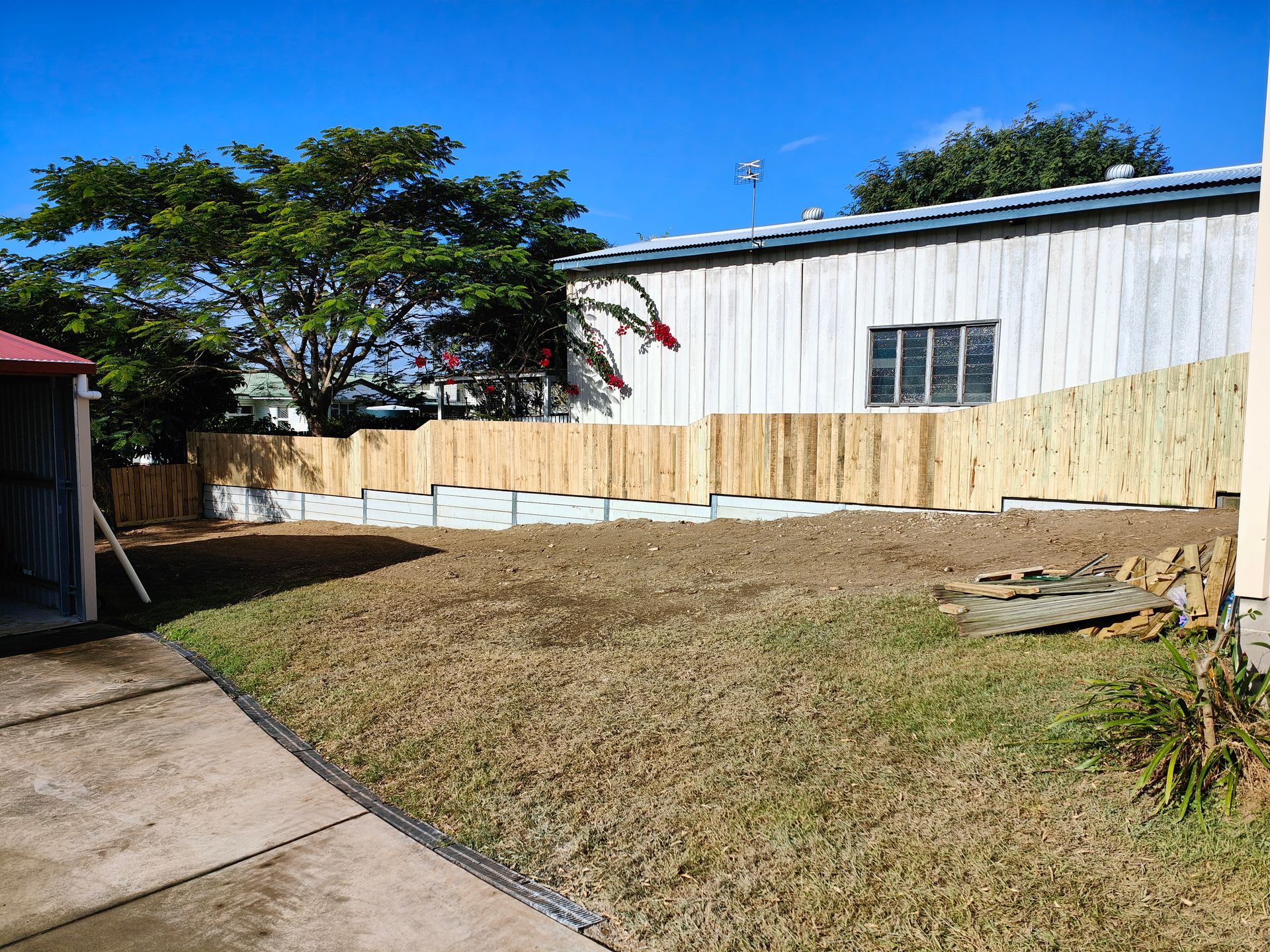 Backyard With Dry Grass, Concrete Patio, Wooden Fence, And White Building Under A Blue Sky — Quality Fences 4 U in Gympie, QLD