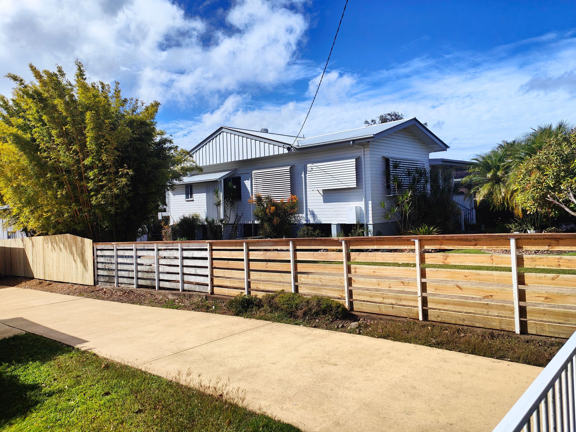 White House Behind A Wooden Fence Beside A Sidewalk Under A Blue Sky With Clouds — Quality Fences 4 U in Gympie, QLD