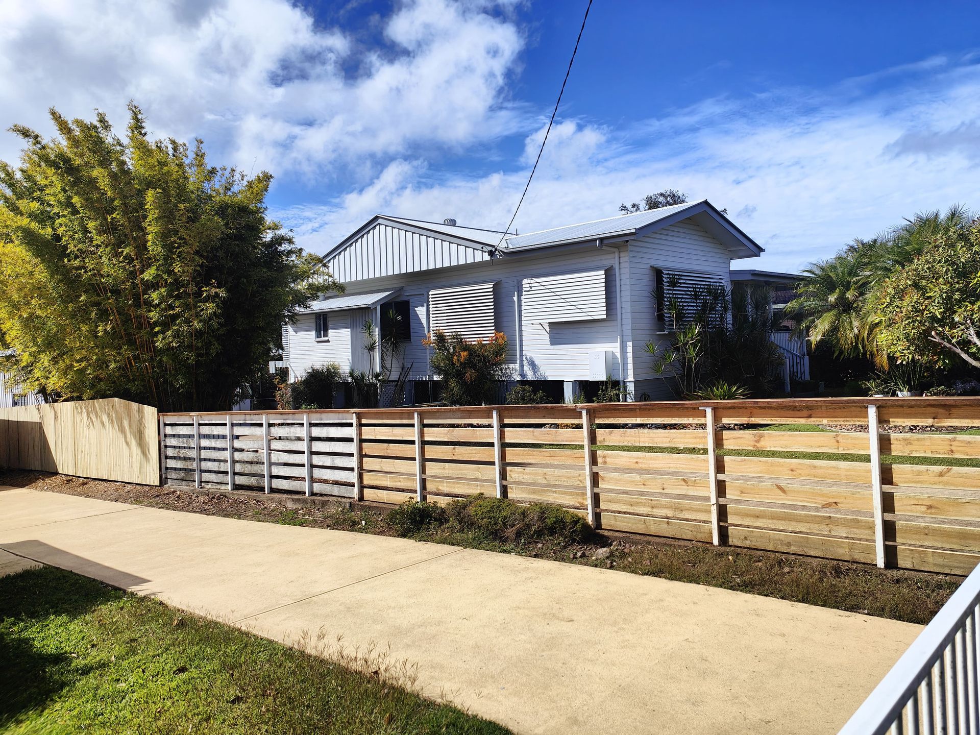 White house with a wooden fence in front, cloudy blue sky — Quality Fences 4 U in Gympie, QLD