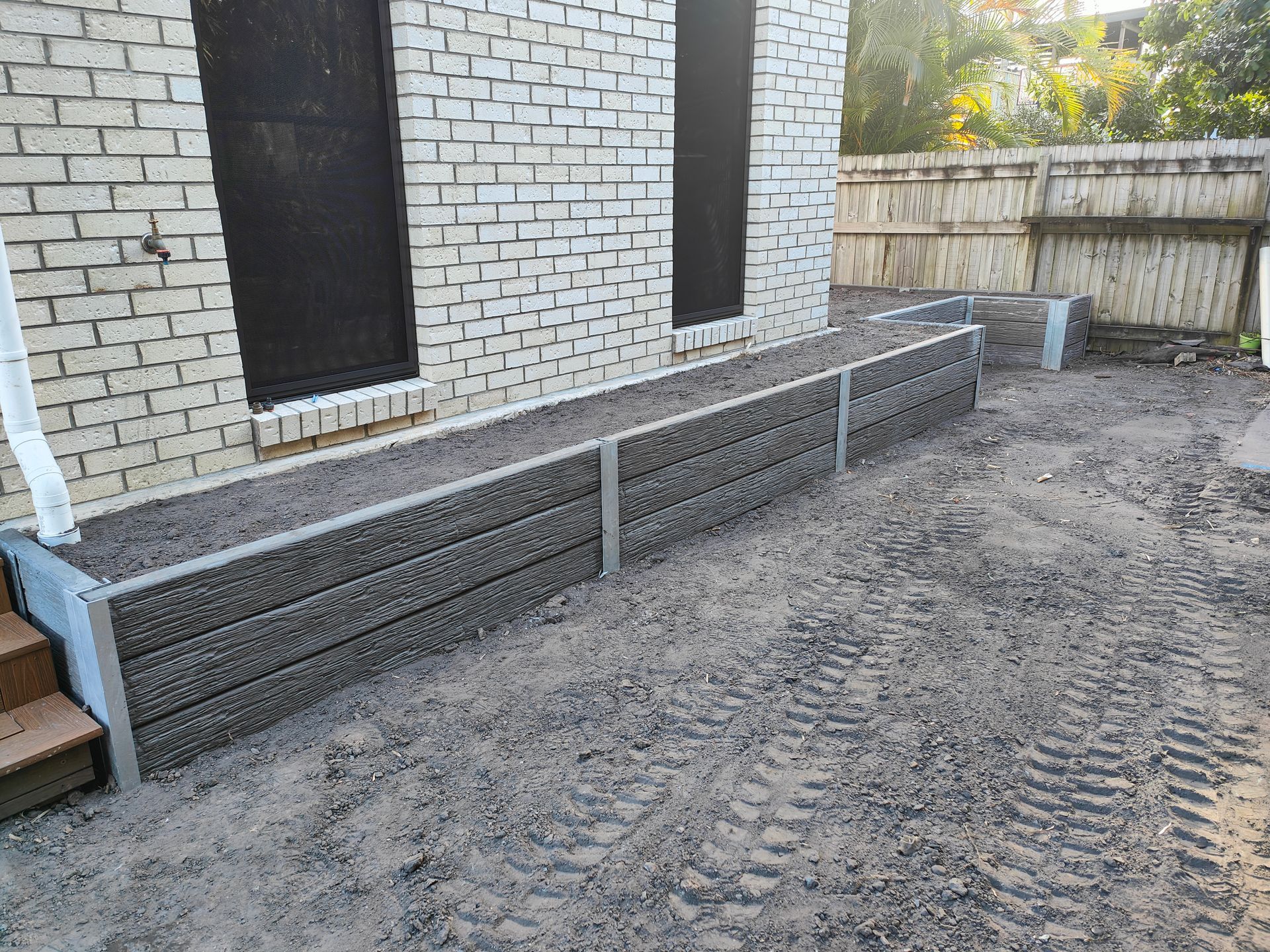 Long Raised Gravel Retaining Wall Beside A White Brick House And Fenced Yard Under Construction — Quality Fences 4 U in Gympie, QLD