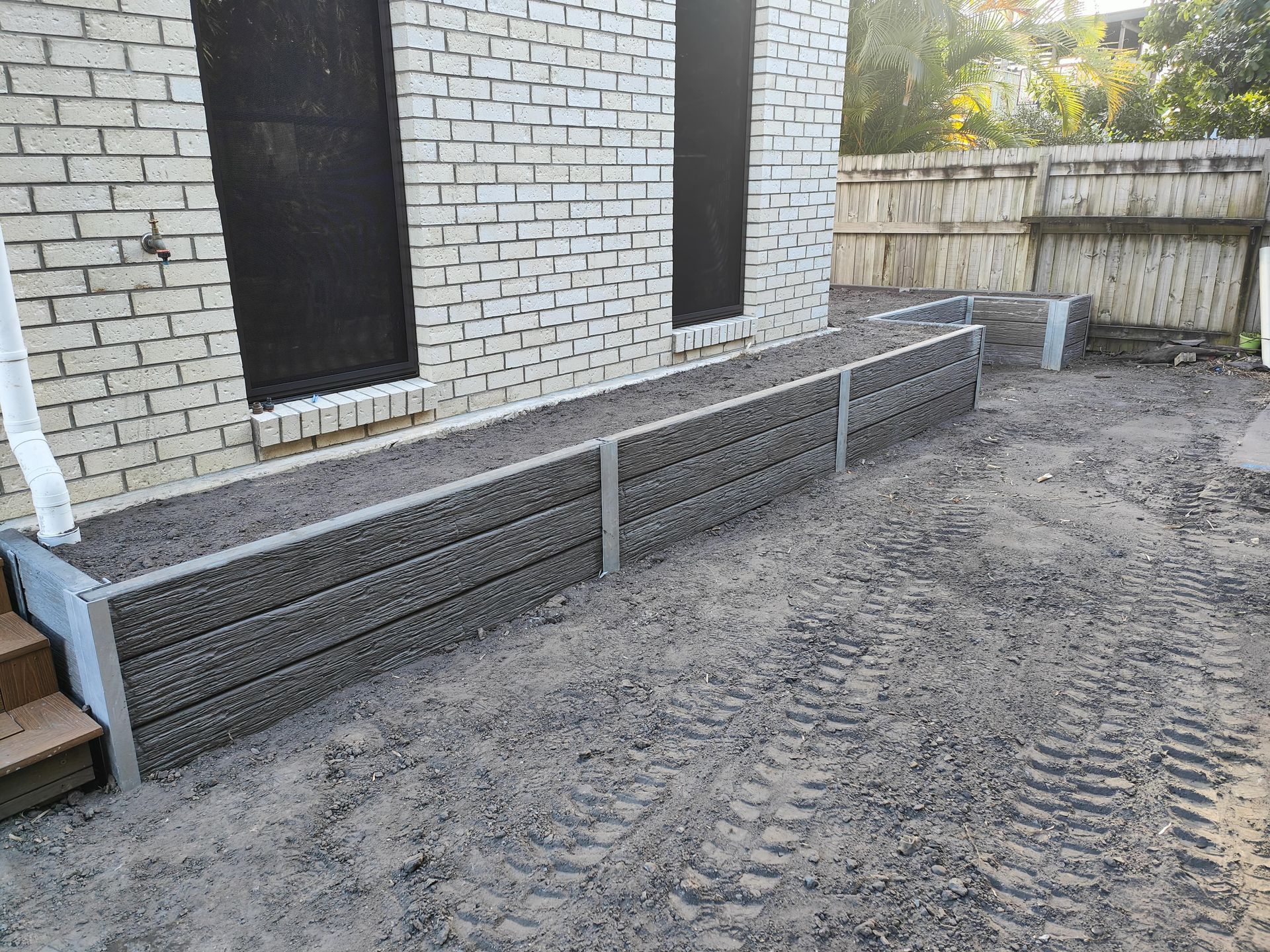 Low retaining wall with gray blocks along a brick building. Gravel ground with tire tracks — Quality Fences 4 U in Gympie, QLD