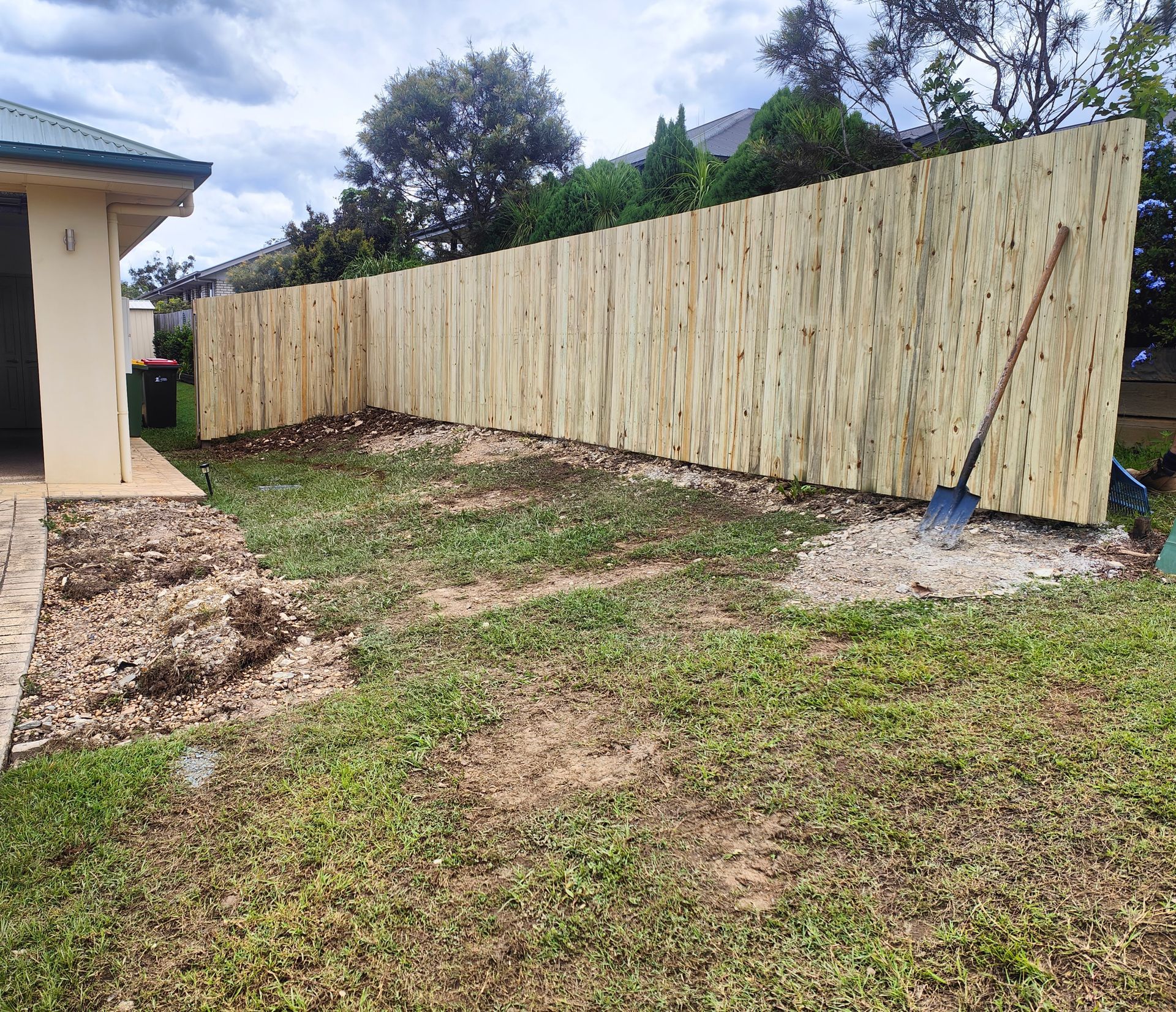 New Wooden Fence Along A Grassy Yard Beside A House, With A Shovel Leaning Against It — Quality Fences 4 U in Gympie, QLD